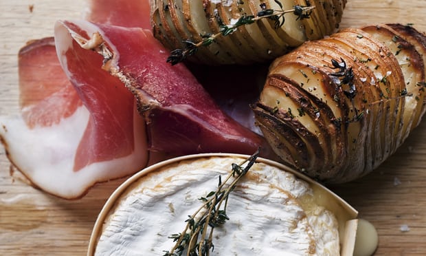 Sliced hasselback potatoes with ham and cheese on a board